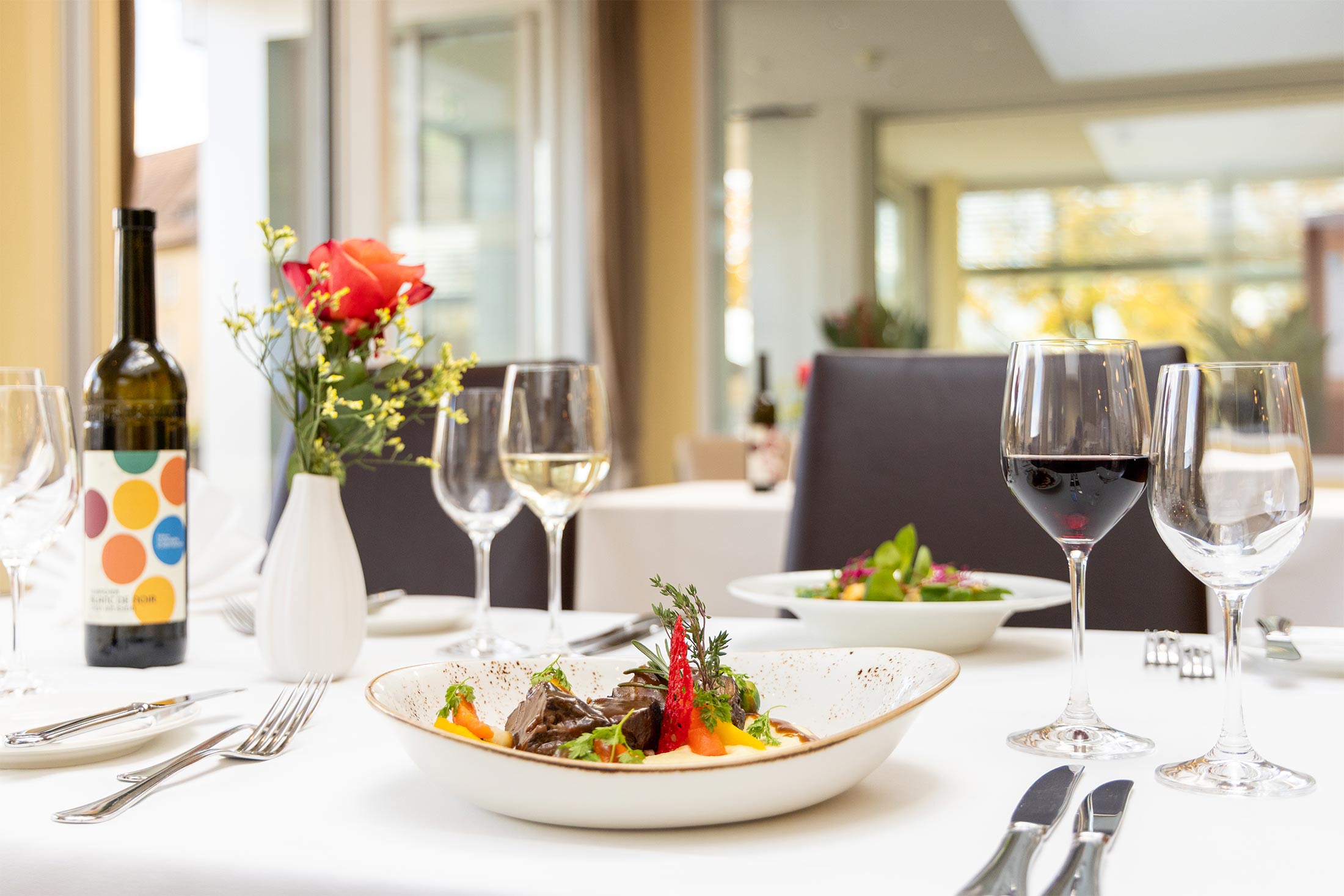Stilvoll gedeckter Tisch im Restaurant mit herbstlichem Gericht und einem Glas des hauseigenen Weins